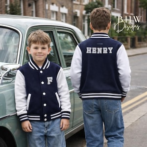 May include: Two children wearing navy blue and white letterman jackets and blue jeans. One jacket has the letter "F" on the front, the other has the name "HENRY" on the back. The jackets have white sleeves and striped cuffs and hems.