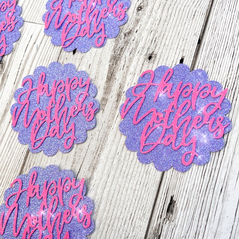Puede incluir: Recortes de papel con purpurina morada con bordes festoneados y el texto "Happy Mother's Day" en letras de purpurina rosa.