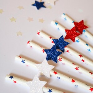 May include: White paper straws with red, blue, and white glitter stars. The straws are decorated with red and blue stars.