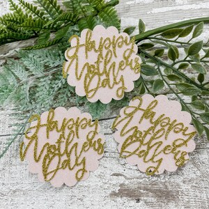 Puede incluir: Tres recortes de papel rosa y dorado con purpurina con el texto "Happy Mother's Day" en letras doradas con purpurina.