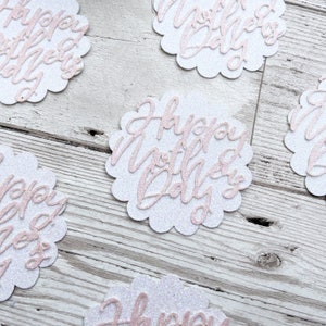 Puede incluir: C&iacute;rculos de papel con purpurina blanca con letras de purpurina rosa que dicen "Happy Mother's Day".