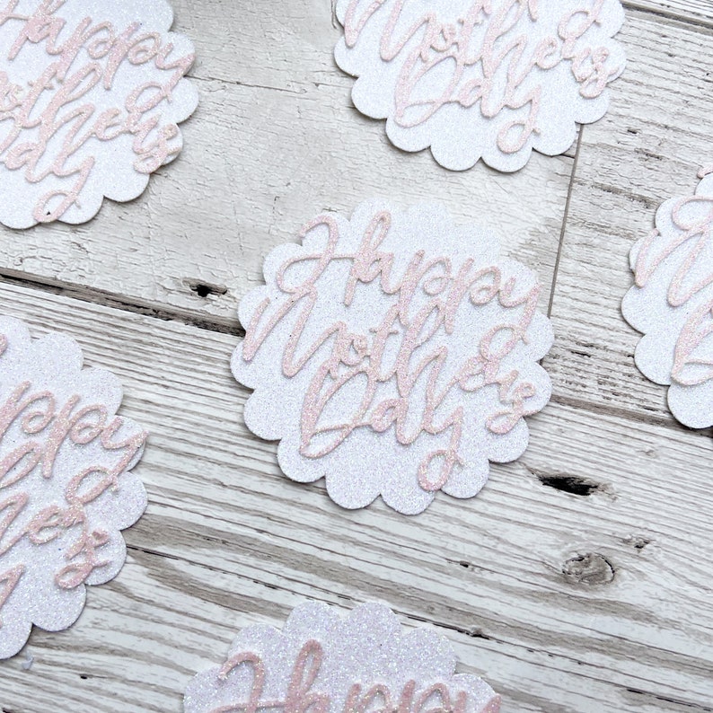 Puede incluir: C&iacute;rculos de papel con purpurina blanca con letras de purpurina rosa que dicen "Happy Mother's Day".
