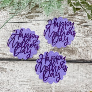 Puede incluir: Tres recortes de papel con purpurina de color morado con el texto "Happy Mother's Day" en una fuente cursiva.