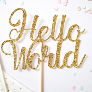Pode incluir: Topo de bolo de glitter dourado com as palavras "Hello World" em fonte cursiva.