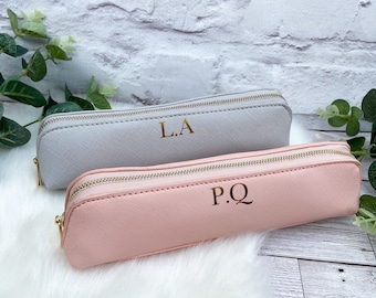 May include: Two zippered pencil cases, one gray and one pink, with gold lettering. The gray case has the initials "L.A." and the pink case has the initials "P.Q."
