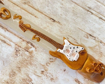 May include: A white and brown mezuzah with a guitar design. The guitar is white with black dots and has a brown body. The mezuzah is made of wood and has a clear plastic tube.