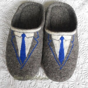 May include: A pair of gray felt slippers with a blue suit and tie design. The slippers have a white collar and a blue tie.
