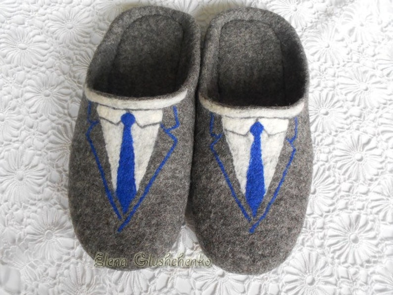 May include: A pair of gray felt slippers with a blue suit and tie design. The slippers have a white collar and a blue tie.