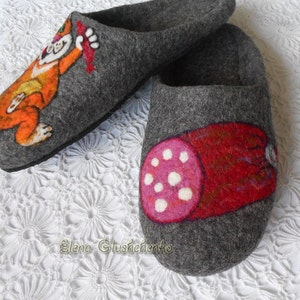 Pu&ograve; includere: Un paio di pantofole in feltro grigio con disegni dipinti a mano. Una pantofola presenta un gatto dei cartoni animati che tiene un salsiccia rossa, mentre l'altra pantofola presenta una salsiccia rossa con pois bianchi.