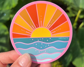 May include: A pink circle sticker with a sunset and ocean scene. The sun is yellow with orange and red rays. The ocean is blue with white waves. The text "HOPE'S PALETTE" is in the lower right corner.