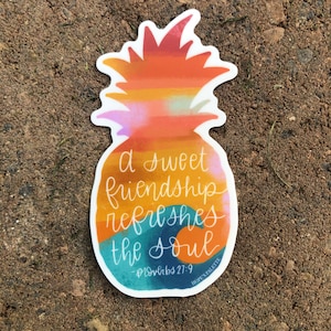 May include: A sticker with a pineapple design and the text "a sweet friendship refreshes the soul - Proverbs 27:9" in a handwritten font. The pineapple is painted in shades of orange, yellow, and pink. The text is in shades of blue and white.