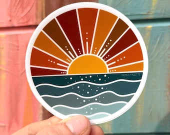May include: A round sticker with a sunset over the ocean. The sun is orange and yellow with red, orange, and brown rays. The ocean is blue and green with white waves. The sticker has the text "HOPE'S PALETTE" in the bottom right corner.