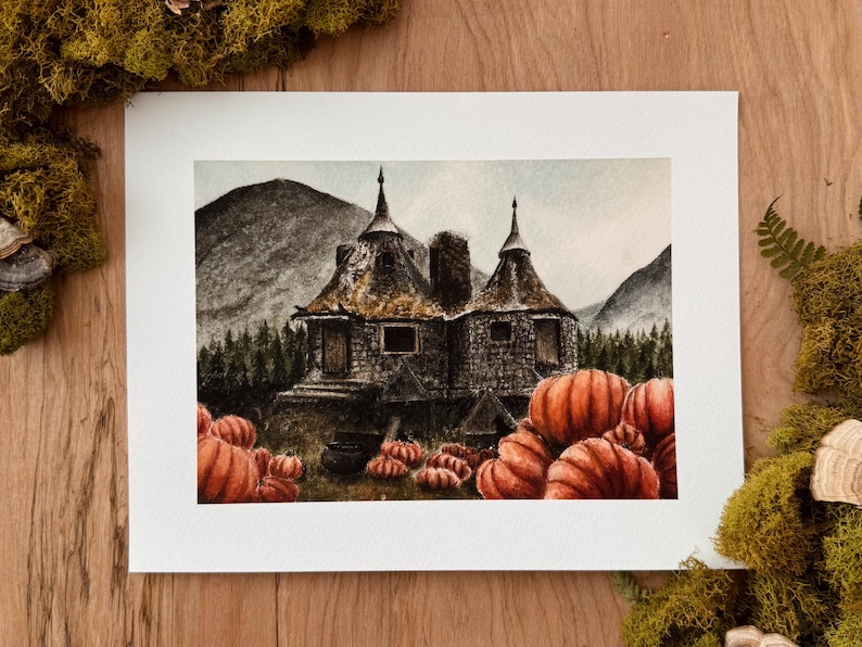 May include: A watercolor painting on paper depicting a stone cottage with two conical roofs nestled in a forest landscape with mountains in the background. Numerous orange pumpkins are scattered in the foreground near the cottage entrance.