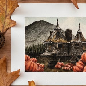 May include: A watercolor painting on white paper depicting a stone cottage with two conical roofs, situated in front of a dark mountain and pine forest. Numerous orange pumpkins are scattered in the foreground, along with a black cauldron.