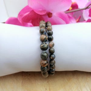 Könnte beinhalten: Ein Armband aus zwei Reihen brauner und schwarzer, gesprenkelter Perlen. Das Armband liegt auf einer weißen Oberfläche.