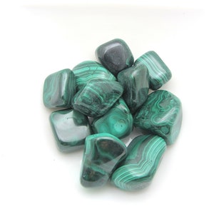 Peut inclure: Une collection de pierres de malachite roulées, chacune avec un motif vert et noir unique. Les pierres sont lisses et polies, avec un aspect naturel et terreux.