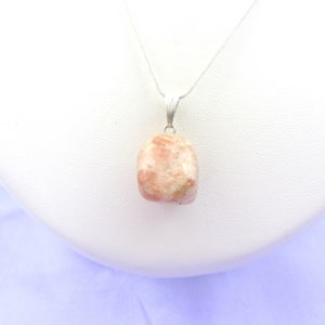 Può includere: Una collana con catena d'argento con un ciondolo in pietra di sole rosa. Il ciondolo è una pietra naturale tagliata grezza di colore rosa chiaro con inclusiones bianche.