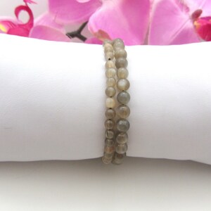 May include: Two grey gemstone bracelets with round beads. The bracelets are stacked on a white surface.