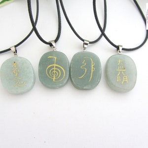 May include: Four green stone pendants with black cords and silver clasps. Each pendant has a different gold symbol or characters. The symbols are "木火土金水", "生命", "气", and "太极".