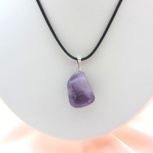 May include: A polished, irregular purple amethyst gemstone pendant suspended from a simple black cord necklace. The stone features natural color variations and is attached to the cord with a small, silver-toned metal bail.