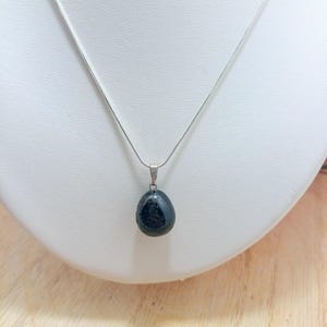 K&ouml;nnte beinhalten: Eine silberne Kettenkette mit einem schwarzen Edelstein-Anh&auml;nger. Der Anh&auml;nger ist glatt und oval.