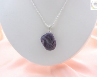 May include: A pendant necklace featuring a polished, irregularly shaped, purple amethyst stone. The stone is suspended from a delicate silver chain. The necklace is displayed on a white bust against a soft pink background.