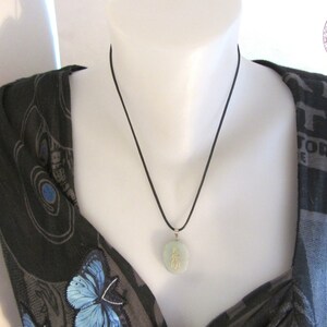 May include: A black cord necklace with a jade green pendant featuring gold Chinese characters. The pendant is round and hangs from a black cord.
