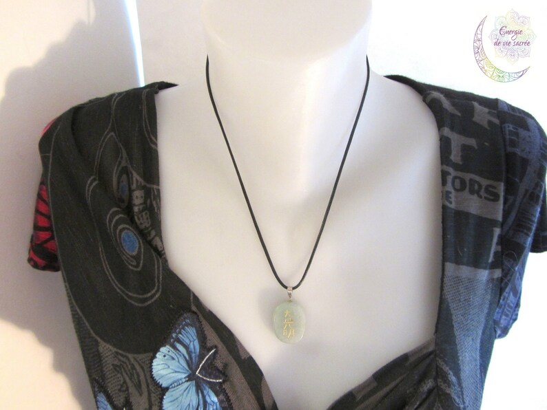 May include: A black cord necklace with a jade green pendant featuring gold Chinese characters. The pendant is round and hangs from a black cord.