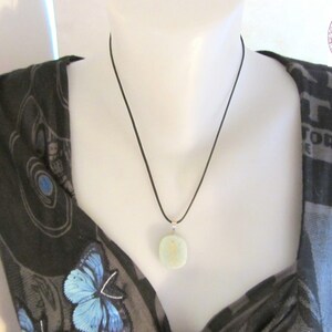 May include: A light green stone pendant necklace with a black cord. The pendant is round and has a smooth, polished surface.