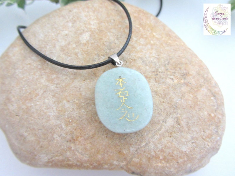 May include: A light green stone pendant necklace with a black cord. The stone has gold lettering that reads "本質", which is Japanese for "essence".