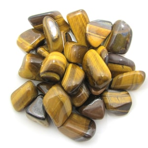 Peut inclure: Un tas de pierres de œil de tigre roulées. Les pierres sont un mélange de brun doré et de noir avec un effet chatoyant et iridescent.