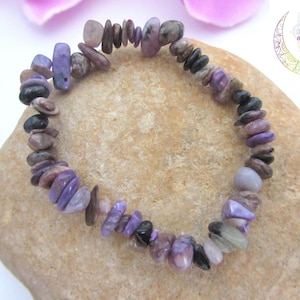 Peut inclure: Un bracelet en pierres violettes et brunes de formes et de tailles variées. Le bracelet est posé sur une roche brun clair. Le texte "Energie de vie sacrée" est visible dans le coin supérieur droit de l'image.