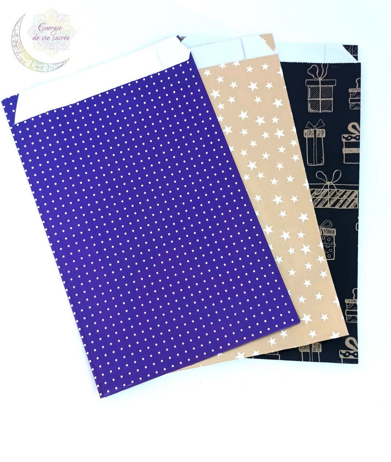 May include: Three rectangular paper envelopes with white adhesive flaps. The first is purple with a white polka dot pattern. The second is tan with a white star pattern. The third is black with a white line drawing pattern of gift boxes.