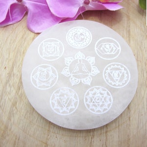 Peut inclure: Plaque de recharge en sélénite blanche avec sept symboles de chakras et une figure méditant au centre.