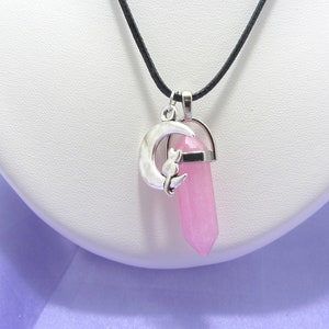 Peut inclure: Un collier avec un cordon noir et un pendentif en forme de croissant de lune argenté orné d'une petite fleur. Un cristal rose en pointe pend du charme.