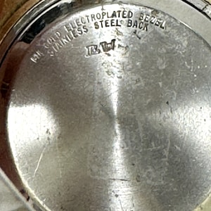 May include: Close-up of the back of a gold-plated watch with the text "14K Gold Electroplated Bezel Stainless Steel Back" engraved on the metal.