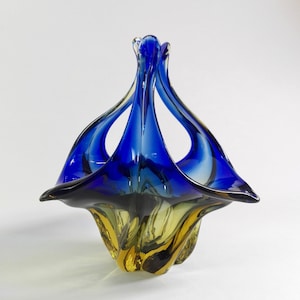 Op de afbeelding: Een blauwe en amberkleurige glazen kom met een uniek, abstract ontwerp. De kom is gemaakt van handgeblazen glas en heeft een delicate, vloeiende vorm.