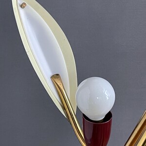 May include: A vintage lamp with a white bulb, a burgundy base, and a gold-toned, curved arm. The lamp has a leaf-shaped, off-white shade with a white interior. The design is reminiscent of the mid-20th century.