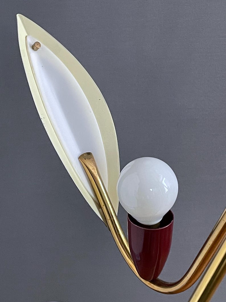 May include: A vintage lamp with a white bulb, a burgundy base, and a gold-toned, curved arm. The lamp has a leaf-shaped, off-white shade with a white interior. The design is reminiscent of the mid-20th century.