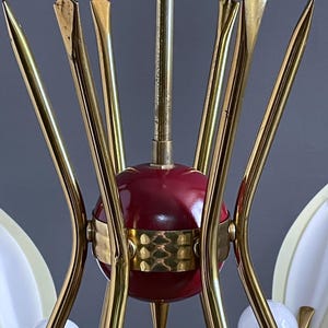 May include: A vintage chandelier featuring a central red sphere, brass-toned metal arms, and decorative details. The light fitting has white, teardrop-shaped shades and small, round light bulbs. The design is reminiscent of mid-century modern styles.