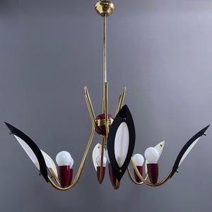 May include: A mid-century style chandelier in gold. It has red, black, and white details, with several light bulbs. The design incorporates leaf-shaped elements and a central red sphere. A stylish lighting fixture.