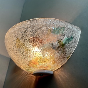 Peut inclure: Applique murale en verre texturé en forme de bol. L'intérieur présente des accents colorés orange, vert et jaune. L'applique est montée sur une base blanche et émet une lumière chaleureuse. Un luminaire décoratif.