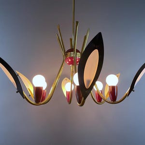 May include: A mid-century chandelier with a brass finish, red accents, and black and white leaf-shaped shades. The light fitting has multiple bulbs and a unique, artistic design, suitable for a living room.