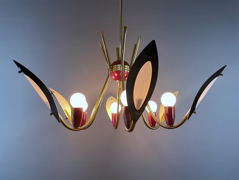 May include: A mid-century chandelier with a brass finish, red accents, and black and white leaf-shaped shades. The light fitting has multiple bulbs and a unique, artistic design, suitable for a living room.