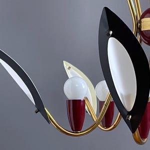 May include: A mid-century modern chandelier with a gold-tone frame. The chandelier features black and white leaf-shaped accents, red accents, and white globe light bulbs. The design is a classic example of mid-century lighting.