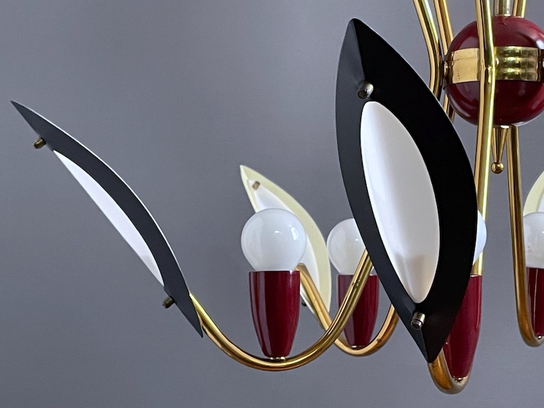 May include: A mid-century modern chandelier with a gold-tone frame. The chandelier features black and white leaf-shaped accents, red accents, and white globe light bulbs. The design is a classic example of mid-century lighting.