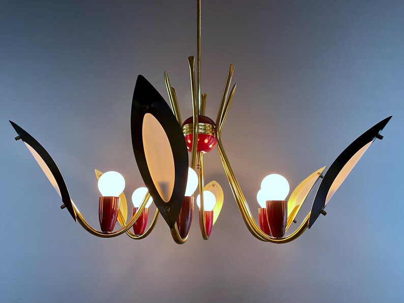 May include: A mid-century modern chandelier with a gold finish, featuring black and cream-coloured leaf-shaped accents. The chandelier has red accents and multiple light bulbs. A stylish lighting fixture for a home.