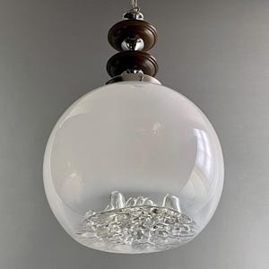 May include: A vintage pendant light fixture with a white globe shade and a decorative, textured glass base. The fixture has a dark brown wooden top with chrome accents and a hanging chain.