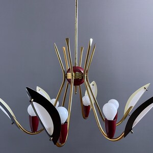 May include: A mid-century modern chandelier with a gold finish, featuring red and black accents. The light fixture has multiple arms with white bulbs and decorative elements, creating a stylish lighting design.