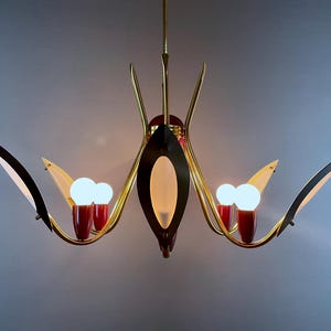 May include: A mid-century chandelier with a gold-tone frame, black accents, and red details. The light fixture has multiple arms with white light bulbs and a central oval-shaped light.
